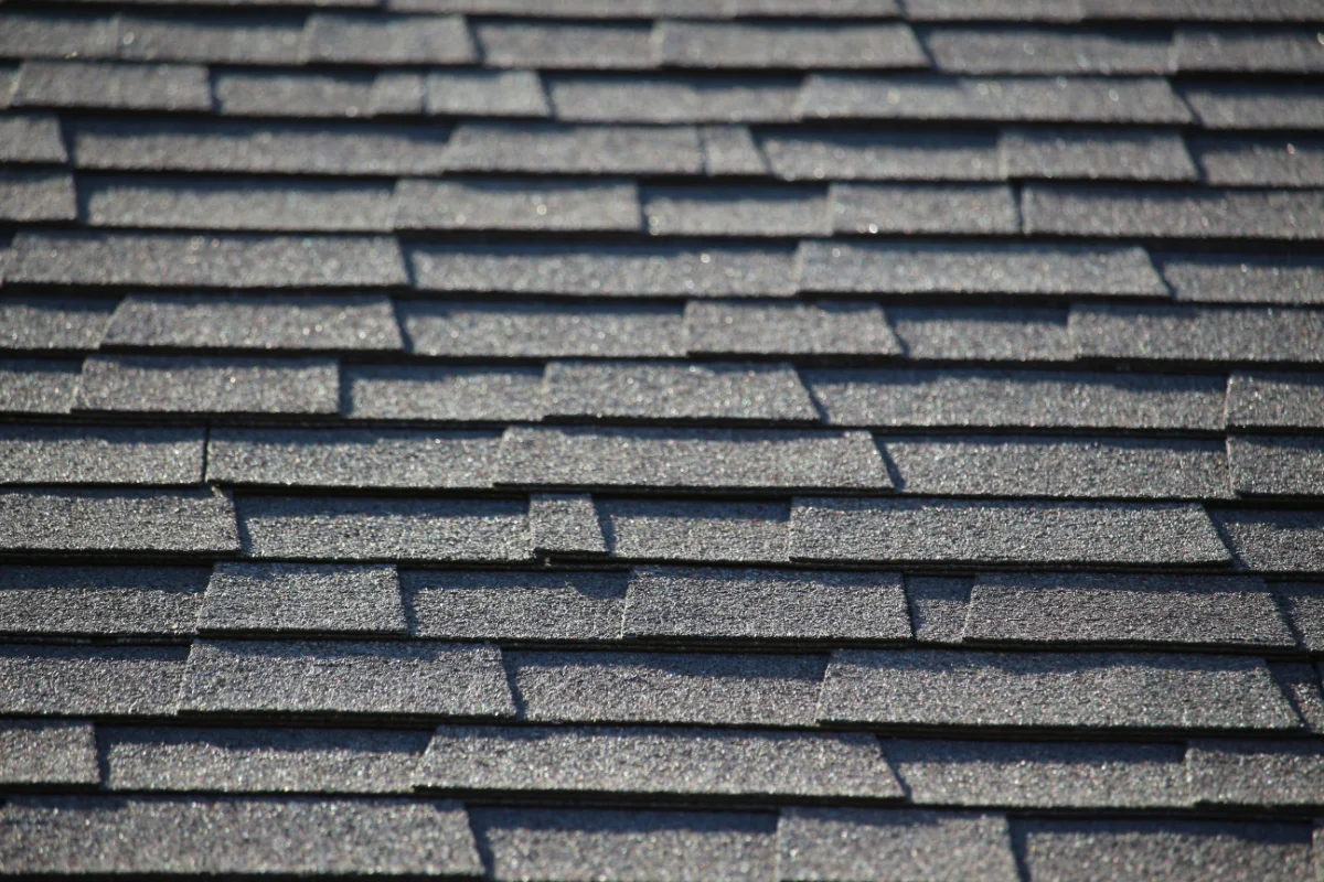 Close-up of overlapping dark gray asphalt shingles on a pitched roof, showing textured, rectangular tabs