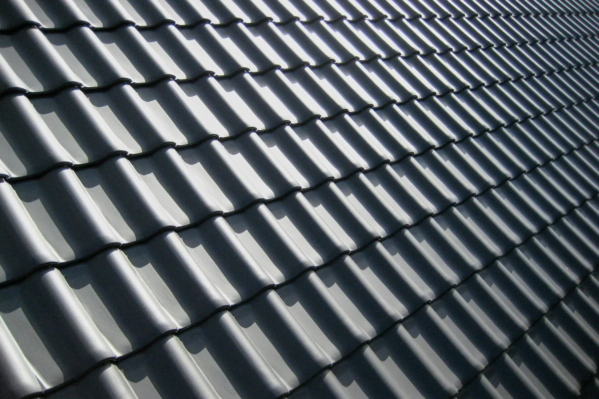Close-up of a grey tiled roof with repeating curved ridges and shadows creating a diagonal pattern, like waves across the surface.
