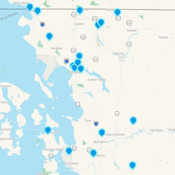 Map showing multiple blue location pins scattered across a coastal region with water on the left and inland towns labeled behind.