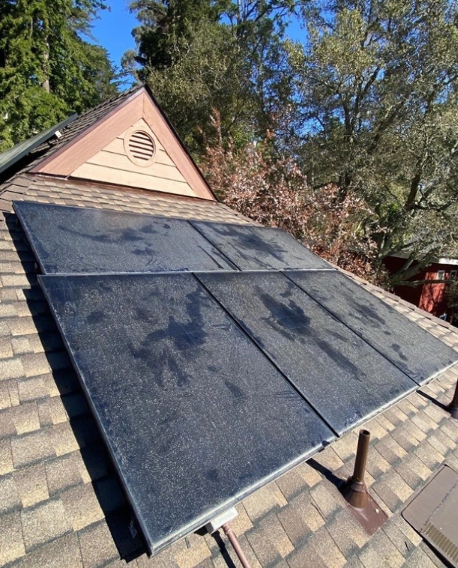 Residential roof with four solar panels installed, blue sky and trees in background.
