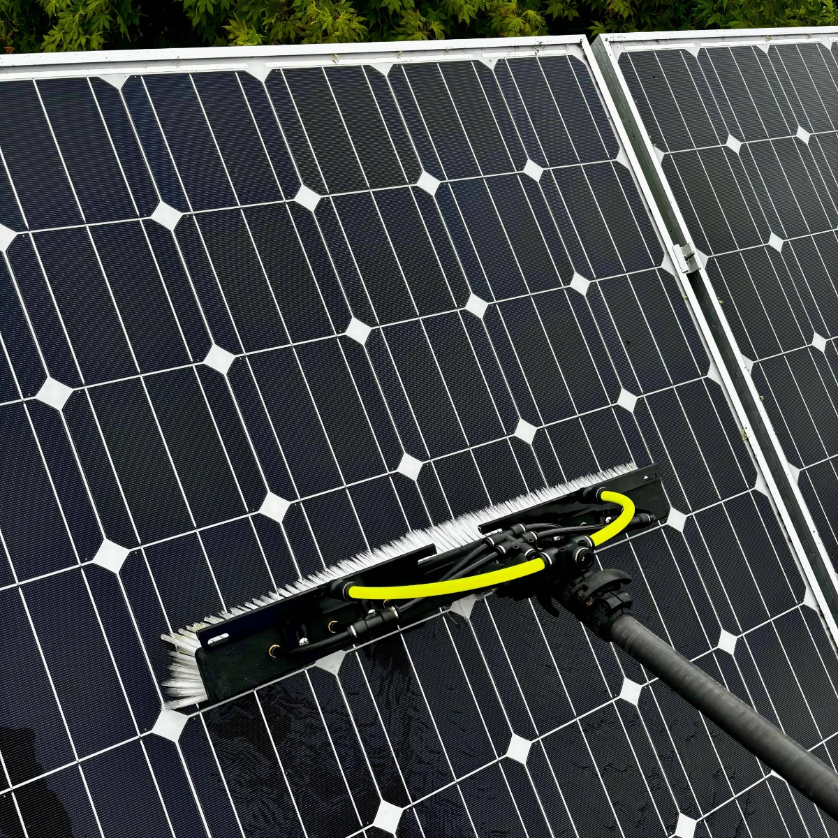 solar-panel-cleaning-img-2 Cleaning solar panels with a long-handled brush connected to a yellow hose or hose attachment at the edge of the panels