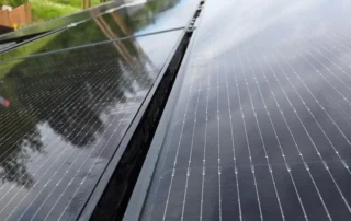 solar-panel-cleaning-img-4 Close-up view of solar photovoltaic panels installed outdoors, showing dark textured surfaces and thin silver grid lines on a roof.